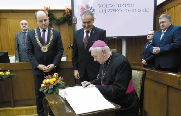 Bp Andrzej Suski dokonuje wpisu do księgi pamiątkowej