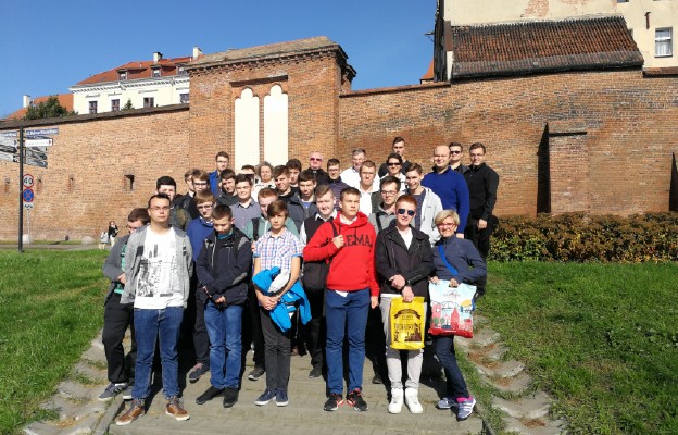 Na tle średniowiecznych murów obronnych miasta Torunia z proboszczem katedry ks. prał. Markiem Rumińskim