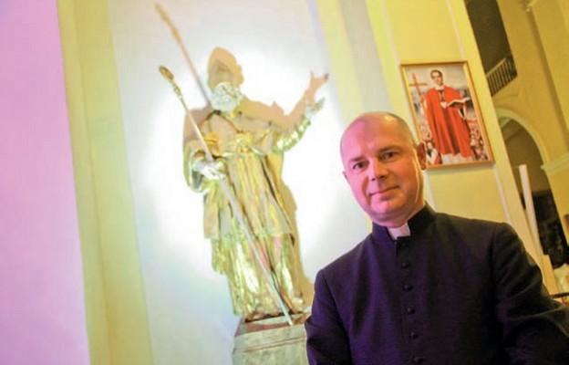 Ks. Stanisław Brasse na tle figury, która przed wojną stała  w głównym ołtarzu dawnego kościoła św. Mikołaja