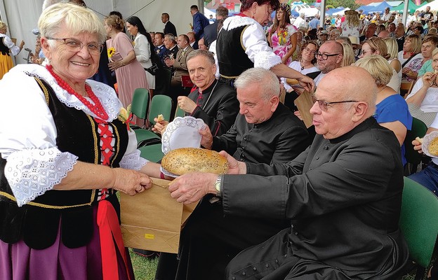 Przedstawicielka zespołu „Ale Babki” Janina Fuja dzieli się dożynkowym chlebem z duchownymi